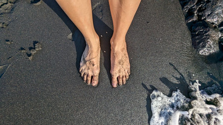 Bare feet of a man in black volcanic sand on a beach. Beaches with which are one of the attractions...