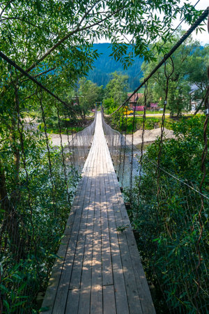 Narrow suspension wooden bridge across the Black Cheremosh River in the village of Verkhovyna. Rural summer landscape. Suspension bridges are one of the attractions of the Carpathians. Ukraine.の写真素材