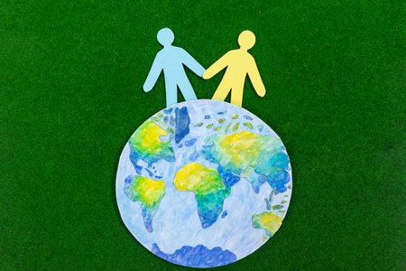 Next to beautiful model of planet Earth on green grass background are figurines of little people. Concepts of ecology and environment, climate change, sustainable development, social responsibility.の写真素材