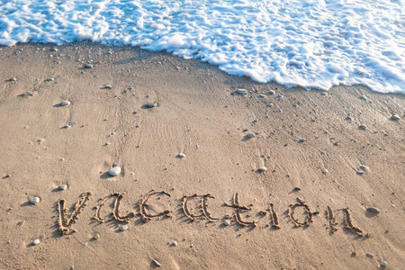 Word "Vacation" on wet sand. Sea foam surf and pebbles on beach at setting sun rays. Natural background close up. Summer rest and vacation.の写真素材