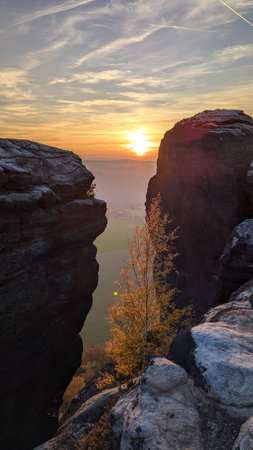 Sun sets between two rounded rocks. Table mountains of Saxon Switzerland National Park. View from observation deck to rocks of Lilienstein hill. Beautiful autumn sunset landscape. Germany.の写真素材