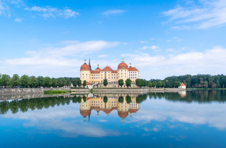 Landscape of beautiful Moritzburg Castle, also known as the Little Pheasant Palace, is reflected in the water surrounding the lake against the blue sky on a sunny day. Saxony. Germany.の写真素材