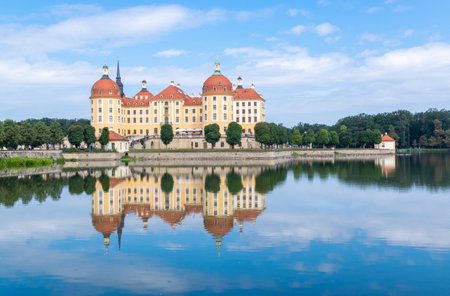 Landscape of beautiful Moritzburg Castle, also known as the Little Pheasant Palace, is reflected in the water surrounding the lake against the blue sky on a sunny day. Saxony. Germany.の写真素材
