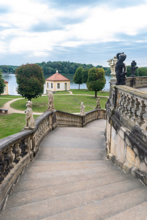 Staircase with sculptures near Moritzburg Castle also known as the Pheasant Palace against a lake surrounding the castle. Blue cloudy sky in the background. Saxony. Germany.の写真素材