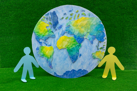Next to beautiful model of planet Earth on green grass background are figurines of little people. Concepts of ecology and environment, climate change, sustainable development, social responsibility.の写真素材