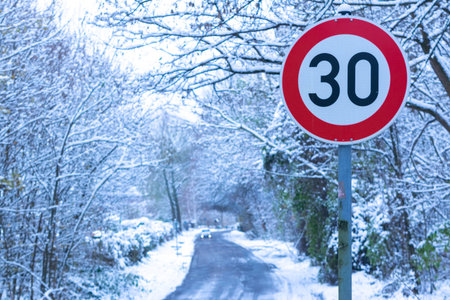 Road sign speed limit 30. Asphalt road covered with ice among snowy forest. Concept of necessity of...