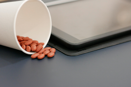 A cup of pills with blur tablet background.の写真素材