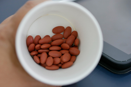 Hand holding cup of pills with blur tablet background.の写真素材