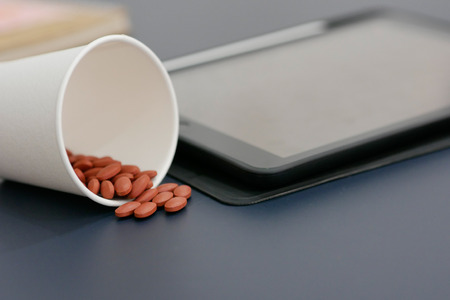 A cup of pills with blur tablet background.の写真素材