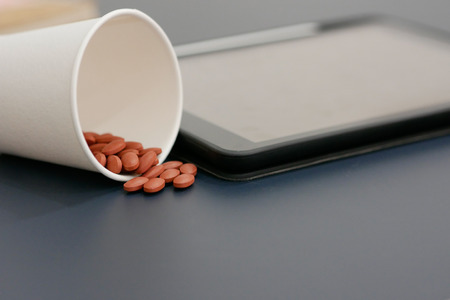 A cup of pills with blur tablet background.の写真素材
