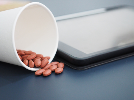 A cup of pills with blur tablet background.の写真素材