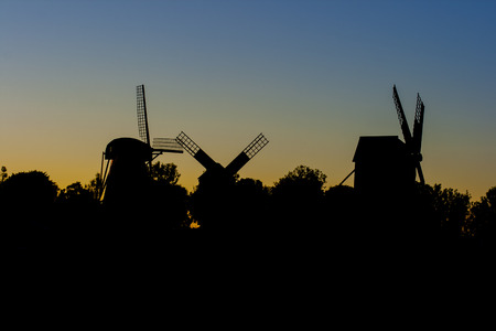 Silhouettes of trees and old windmills during sunsetの写真素材