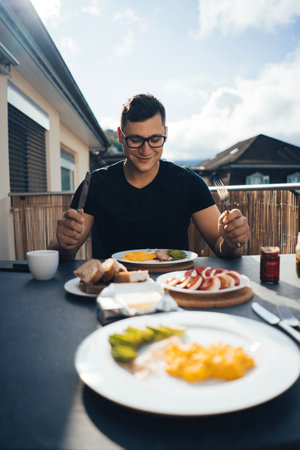 Man having breakfast on the balcony in the fresh air. Scrambled eggs, mozzarella, tomatoes, avocado...