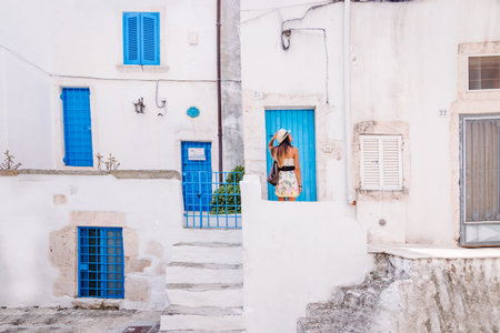 Young female traveler with straw hat in Ostuni in front of a typical Apulian house with blue colored doors and windowsのeditorial素材