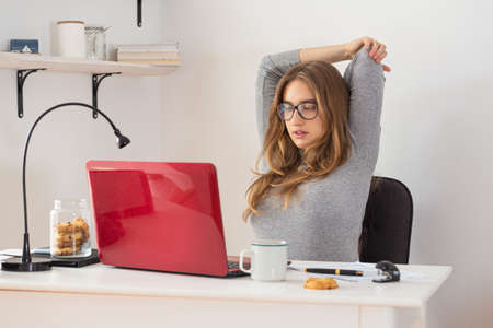 Beautiful natural blonde woman stretching in front of the laptop. Home remote working. Relax time. Isolation time. Pandemic threat. Virus outbreak implications.の写真素材