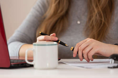 Woman writing her signature on sheet of paper close-up. Remote work from home.の写真素材
