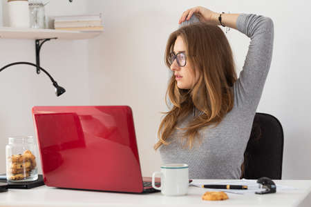 Remote classes. Natural blonde woman stretching in front of her laptop. Working at desk. Pandemic threat. Isolation time. Virus outbreak implications.の写真素材