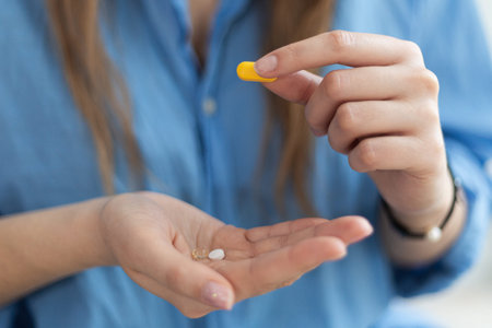 Close-up of woman's hands holding yellow medical pill against blue shirt. Coronavirus disease outbreak.の写真素材