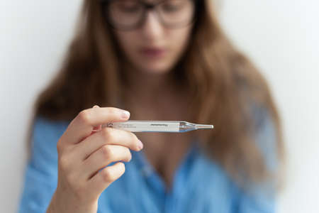 Close-up of medical fever thermometer being held by blonde woman showing high temperature. Virus disease outbreak.の写真素材