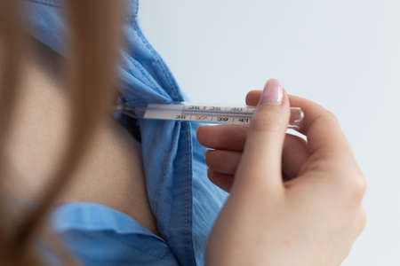 Blonde woman checking temperature with thermometer. Close-up. Coronavirus threat. White background.の写真素材