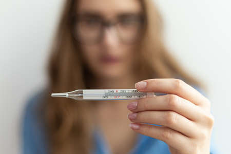 Medical thermometer showing high temperature close-up being held by young blonde woman.の写真素材
