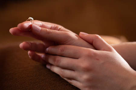 Woman holding golden ring in her fingers, Close-up on hands. Blurry background.の写真素材