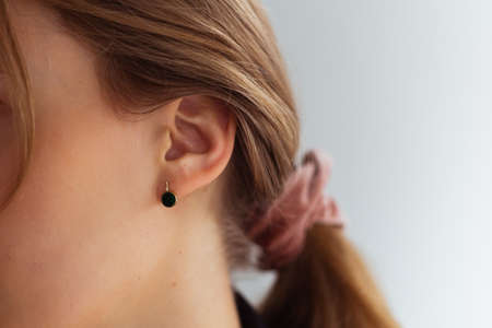 Golden earring with green stone against hair tied up in a ponytailの写真素材