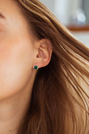 Gold earring with green gemstone close-up. Blonde flowing hair. Blurry background. Beauty routineの写真素材