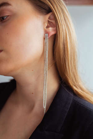 Blond caucasian woman with perfect skin looking down with long diamond earrings, Black jacket, elegant dress, business outfit, white backgroundの写真素材