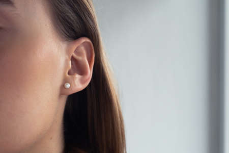 Small pearl earring on a young blonde woman with perfect skin. Close-up. Isolated.の写真素材
