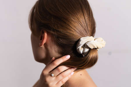 Natural blond woman holding her amazing hair in ponytail with beige scrunchie. Side perspective. White background.の写真素材