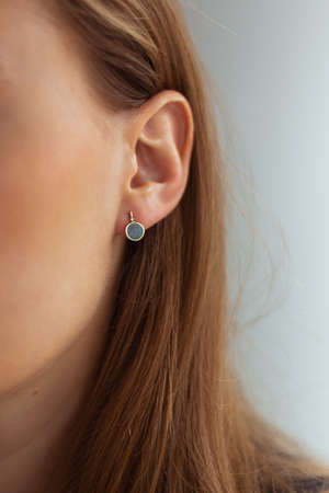 Small golden earring with green malachite on a young blonde woman with perfect skin. Close-up. Isolated.の写真素材