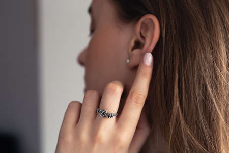 Young blonde woman touching her ear with her finger with silver ring, painted in nude short nails,の写真素材