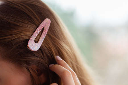 Close up of a cute, pink, girly hairpin on a blonde hair. Blurry background. Beauty, fashion, teenageの写真素材