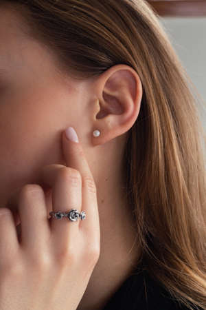 Woman's ear close-up. Pearl earring, natural blonde woman touching her face with painted light pink nail,の写真素材