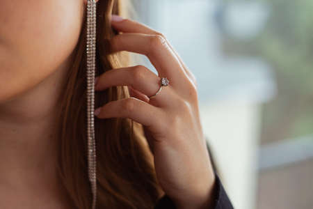 Diamond ring on woman's finger, long earring in the background, hand touching hair, close-up Blond hair, beauty routineの写真素材