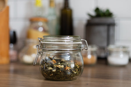 Small glass jar with green tea, healthy breakfast preparation, rustic style interior design, medical herb, blurry background, bright kitchenの写真素材