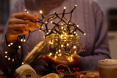 Woman holding glass jar with warm gold christmas lights and rustic style handmade, handcrafted diy ornaments and decorations, wearing purple winter cable knit sweater, blurry backgroundの写真素材
