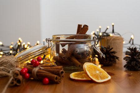 Glass jar with cinnamon sticks inside, with many christmas rustic style, handmade diy ornaments, blurry light in the background, warm tones and winter mood, front viewの写真素材