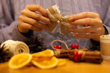 Woman doing diy, handmade christmas bows rustic style ornaments, decorations, purple cable knit sweater, winter mood, warm tones with blurry foreground.の写真素材