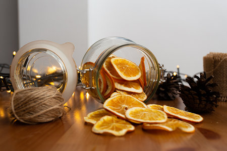 Rustic style christmas diy, handcrafted, handmade ornaments and decorations, cinnamon stick and dried oranges falling from glass jar with lights in the background, front viewの写真素材