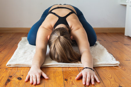 Fit woman doing yoga pose on the floor. Stretching in home. Diet routine. Body positive. View from the front.の写真素材