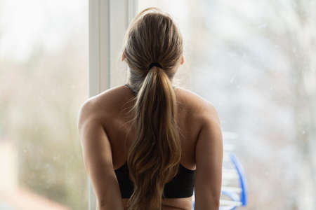 Young blonde woman stretching at home, sport exercises, view from the back. Spring time workout. Body positive.の写真素材
