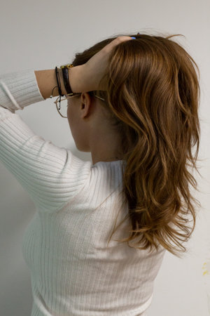 Young healthy woman holding her long, blond, wavy hair on the back of her head, hair is reflecting lights, model on a white wall from the sideの写真素材