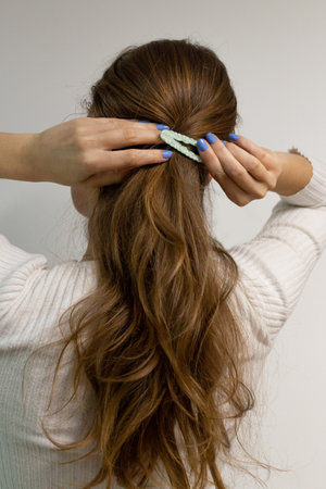 Young woman clipping her blond hair with a snap hair clip with little flowers on it, photo on a white backgroundの写真素材
