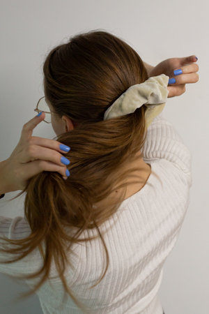 Caucasian blonde woman making a ponytail with a white scrunchy in a white blouse on a white background, photo in movementの写真素材