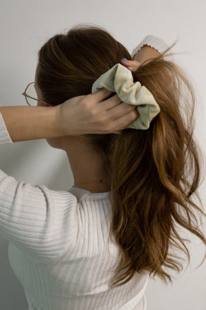 Caucasian woman making a high ponytail with a beige scrunchy, posing from the back, white backgroundの写真素材