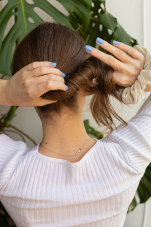 Blonde woman in the process of making sleek low bun, focus on slim neck, hands, fingers and nails, view from behindの写真素材
