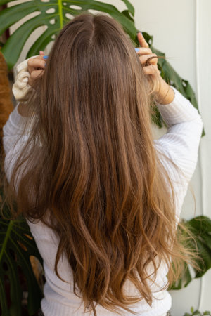Natural blonde woman fixing her long hair and touching her head in a gently way. Top view, arms raised, hair in movement. Plants in the background.の写真素材