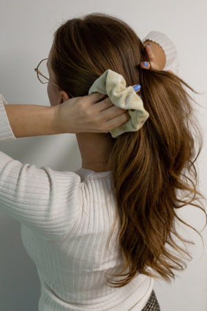Young woman doing a ponytail with beige hair tie, scrunchie, view from the back against white background.の写真素材